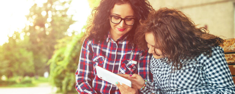 Two women in flannels looking at tablet outside
