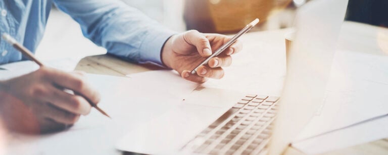 Person using laptop, phone, and pencil
